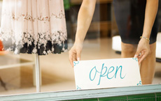 woman placing an open sign in the front window of a retail business