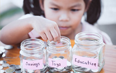 little girl counting coins into savings jars with different labels